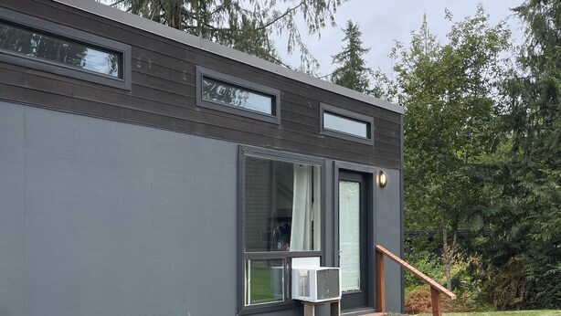 A modern building with a grey exterior, a small outdoor seating area with two chairs and a table, and a staircase leading to a door. - Charming Tiny House Retreat (Olympia)