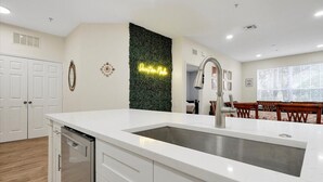 A modern kitchen with a white countertop, stainless steel sink, and a green vertical garden wall. - Windsor Hills  Charming 3BR Condo, Pool, By Disney (Kissimmee)