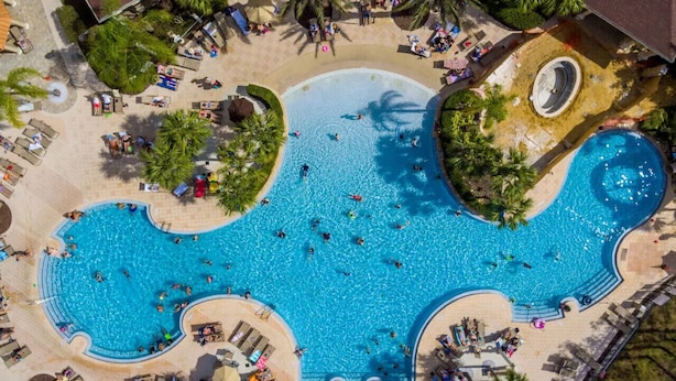 A large outdoor swimming pool with multiple lanes, surrounded by palm trees and sun loungers. - Windsor Hills  Charming 3BR Condo, Pool, By Disney (Kissimmee)