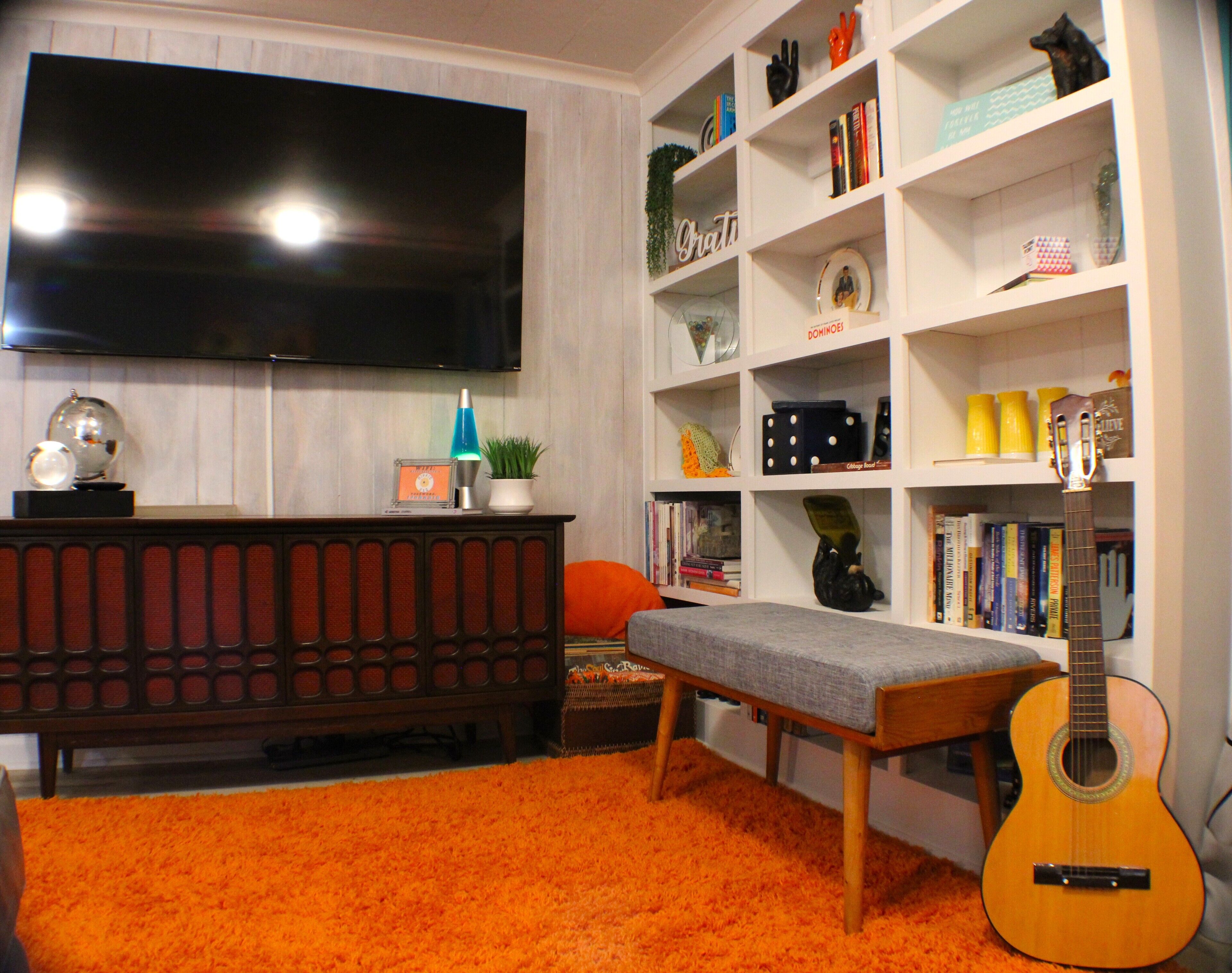 A living room with a television, bookshelf, and a guitar.