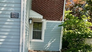 A house with a side door labeled "HIPPIES USE SIDE DOOR" and a small outdoor seating area with a table and a fire pit.