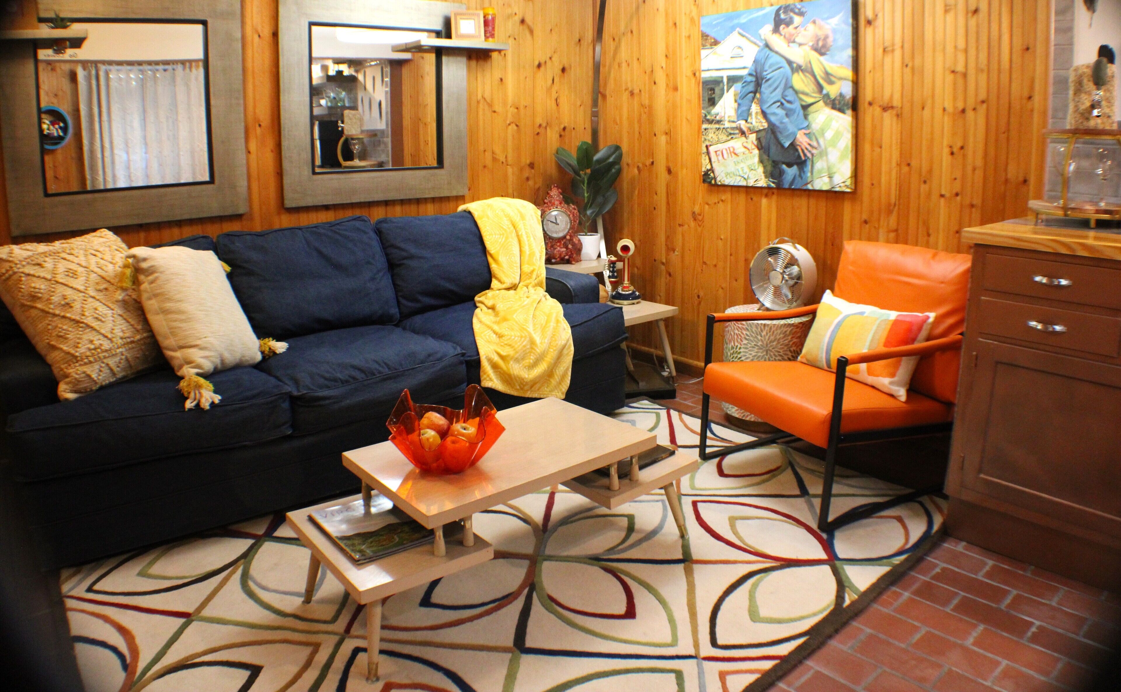 A cozy living room with a blue sofa, orange armchair, and a coffee table with a bowl of fruit.