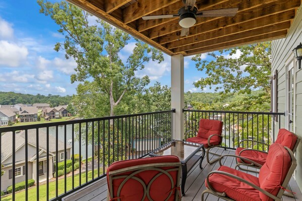 A covered porch with a view of a lake, red chairs, and a ceiling fan.