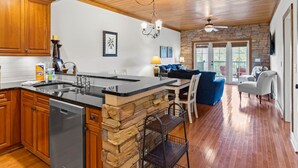 A kitchen with wooden cabinets, a stone accent wall, a black countertop, and a built-in dishwasher.