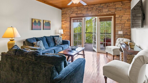 A cozy living room with a stone wall, wooden ceiling, and a ceiling fan. There are two sofas, a coffee table, and a chair.