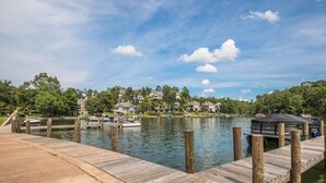 A lakeside dock with boats, a covered area, and houses in the background.