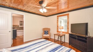 Une chambre à coucher comprenant un lit, un téléviseur, un ventilateur de plafond et donnant sur une salle de bain.