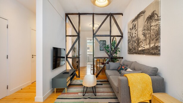 Een moderne woonkamer met een grijze bank, een gele plaid en een televisie op een meubel.