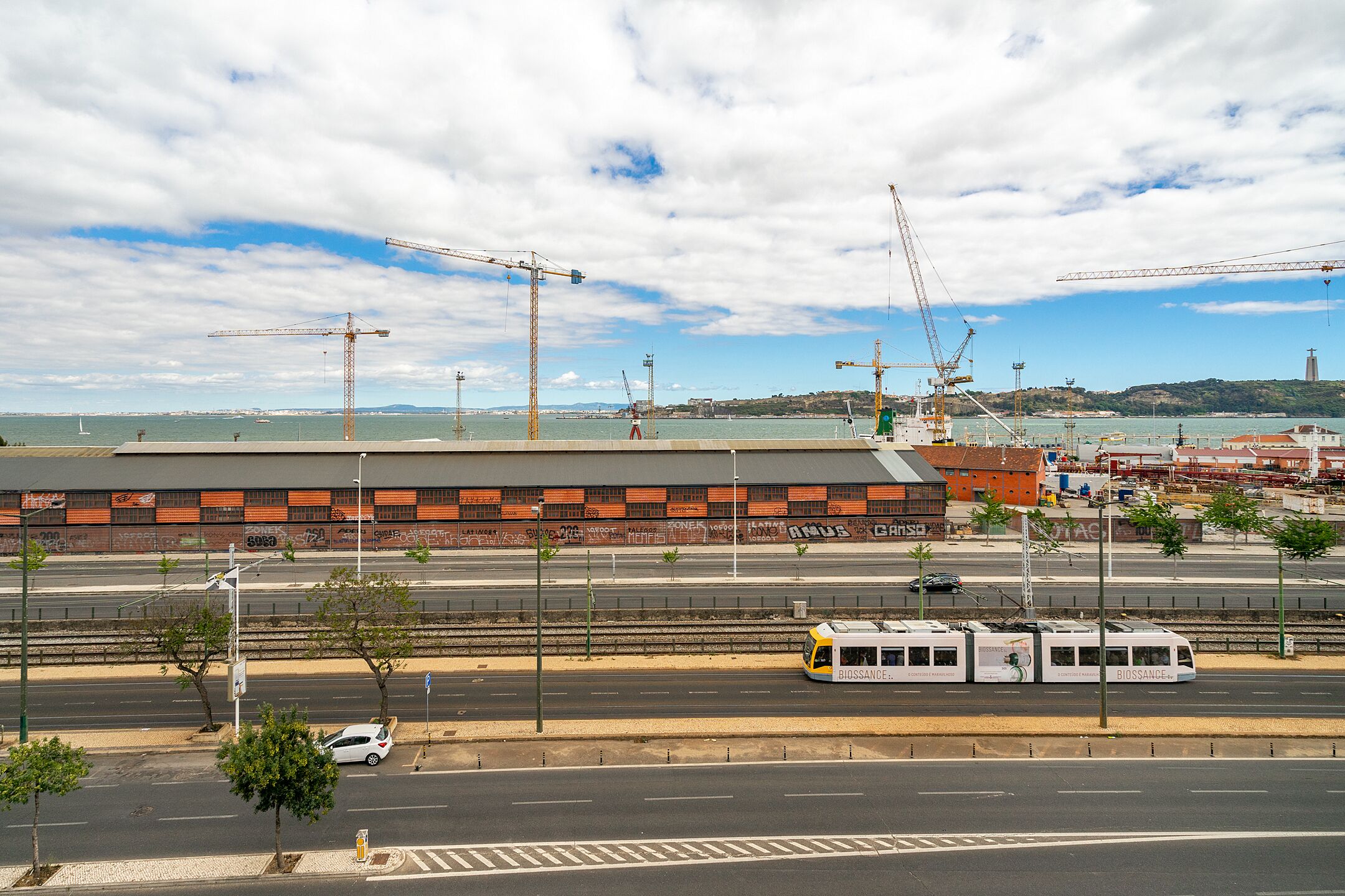 A tram on a track, a bridge, and a building with graffiti.