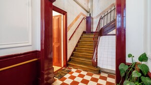 Una escalera con piso a cuadros, barandal de madera y una puerta roja en la parte superior.