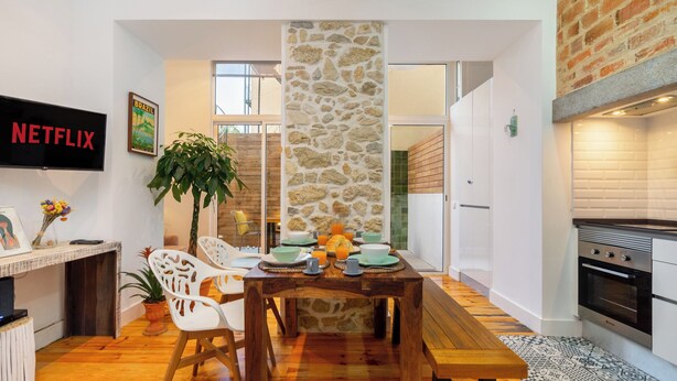 Una sala moderna con una pared de acento de piedra, una mesa de comedor con platos y una planta, y una cocina con pared de ladrillo y electrodomésticos.