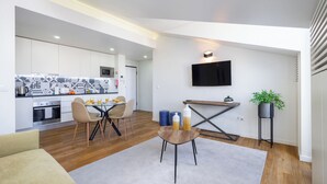 A modern kitchen with white cabinets, a dining area with a table and chairs, a TV mounted on the wall, and a potted plant. - Alcântara Premium Apartment (Lisbon)