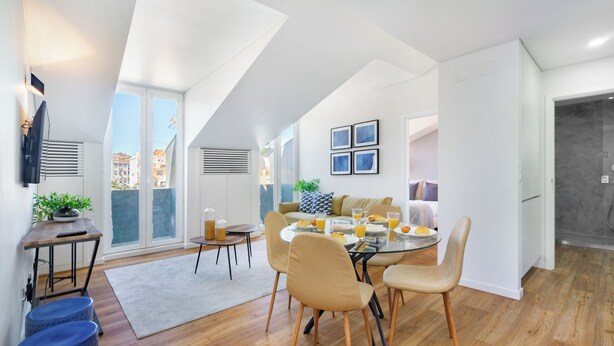 A modern kitchen with a dining area, featuring a round table, chairs, and a view of the city through large windows. - Alcântara Premium Apartment (Lisbon)