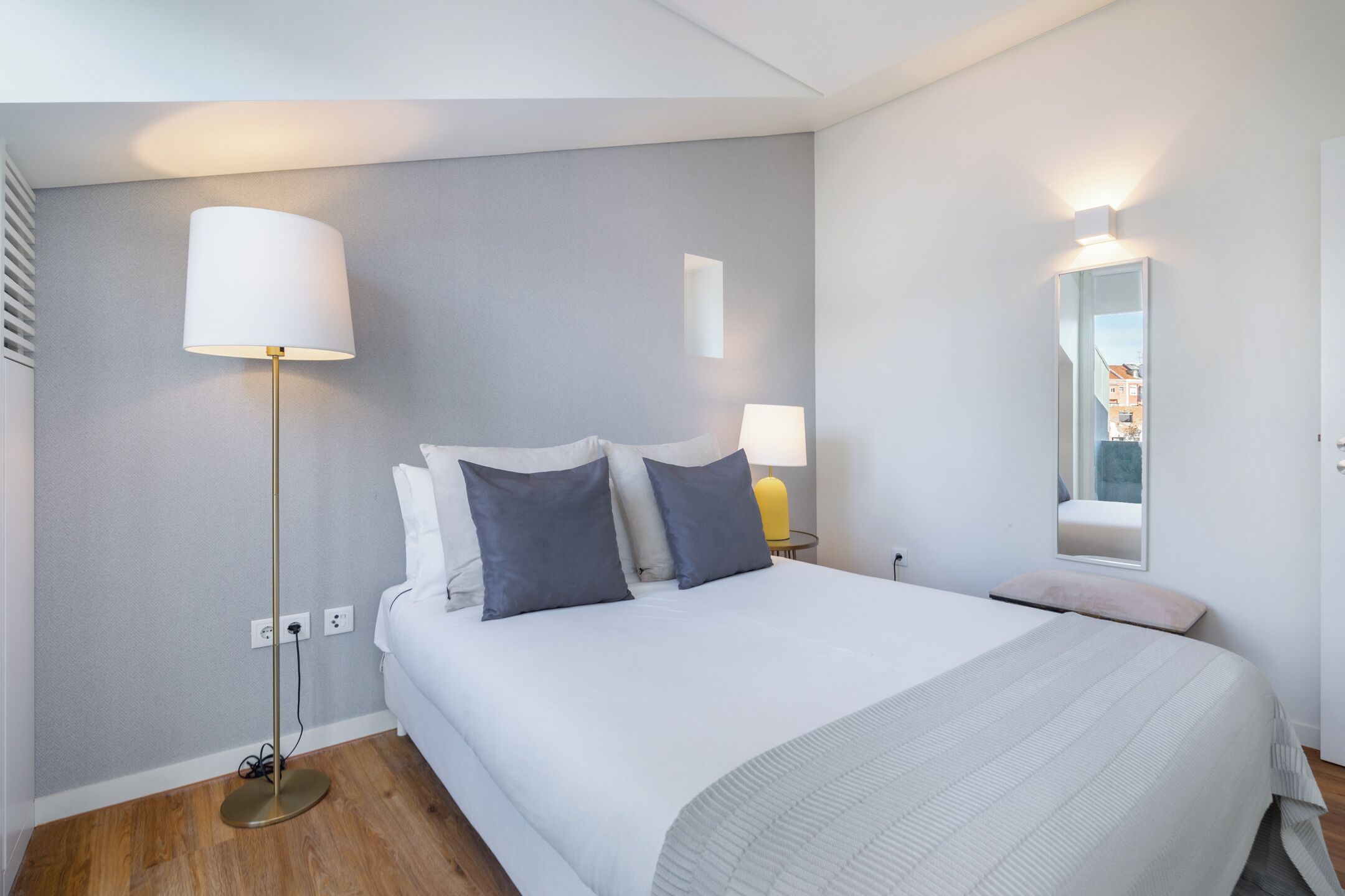 Una habitación de hotel moderna con una cama grande, dos lámparas de noche, un espejo y una mesita.