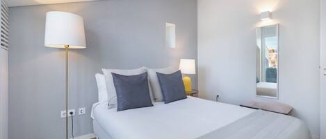 Una habitación de hotel moderna con una cama grande, dos lámparas de noche, un espejo y una mesita.