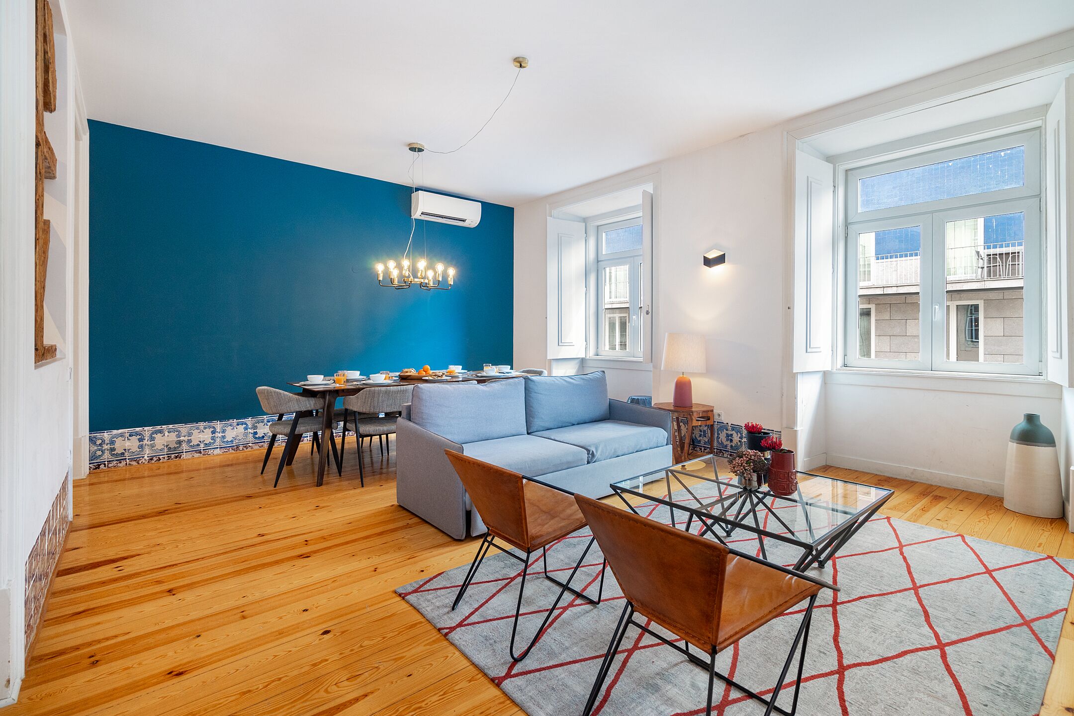 A modern living room with a blue accent wall, a sofa, a glass coffee table, and a dining area with a table and chairs.