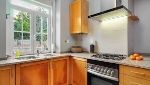A kitchen with wooden cabinets, a gas stove, and a window with a view of greenery. - Aq2 Prime Location Luxury For Family & Friends (Lisbon)