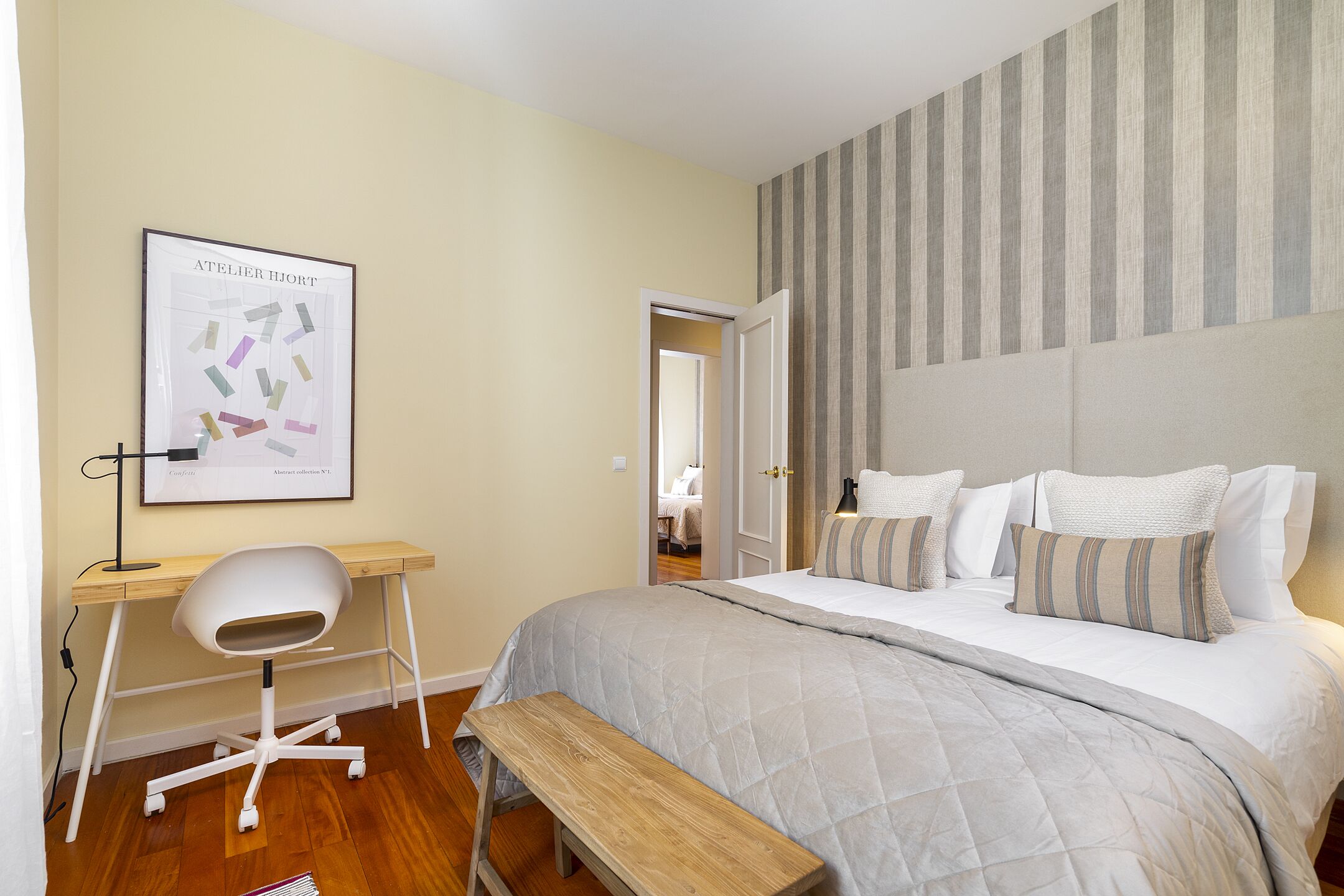 A bedroom with a bed, bedside table, chair, and a desk with a chair.