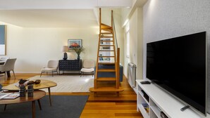 A modern living room with a large flat-screen TV, a wooden ladder, and a bookshelf. - Luxury Lisbon Penthouse: Designer Decor & Epic Views (Lisbon)