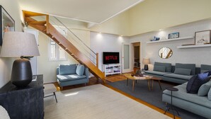 A modern living room with a wooden staircase, a flat-screen TV, and a sofa set. - Luxury Lisbon Penthouse: Designer Decor & Epic Views (Lisbon)