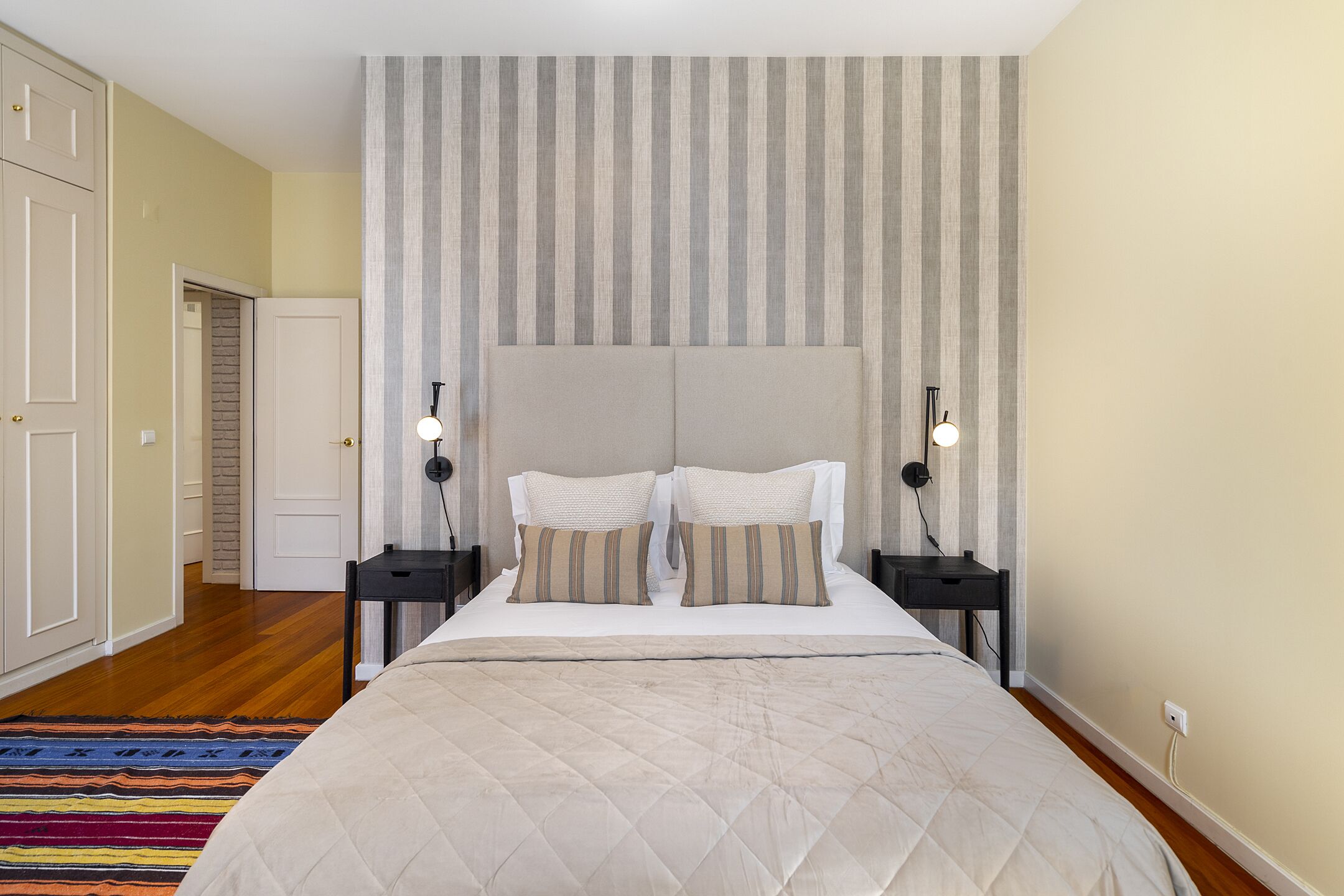 Een slaapkamer met een groot bed, gestreept behang en een houten vloer.