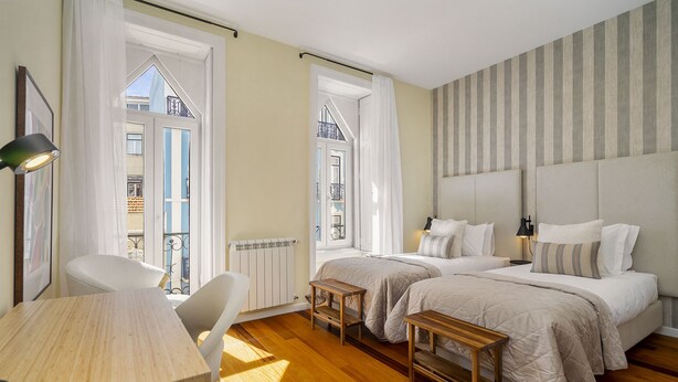 A hotel room with two beds, a wooden table, a chair, and a view of the outside balcony. - Luxury Lisbon Penthouse: Designer Decor & Epic Views (Lisbon)