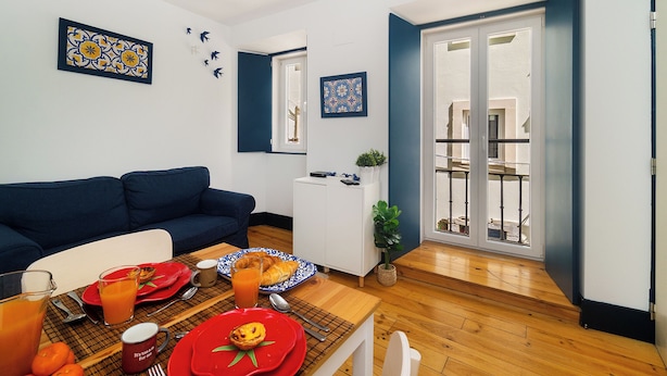 A modern living room with a blue sofa, a dining table set with plates, glasses, and a plant.