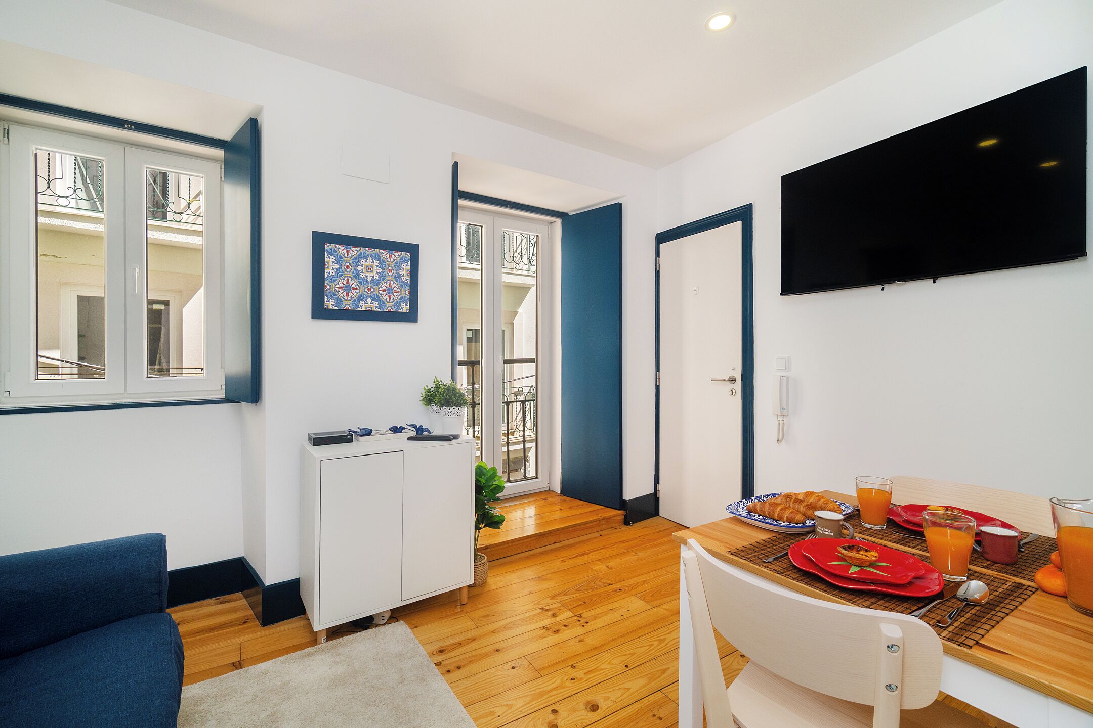 Eine moderne Küche mit Essbereich, einem an der Wand befestigten Fernseher und Blick auf den Balkon.
