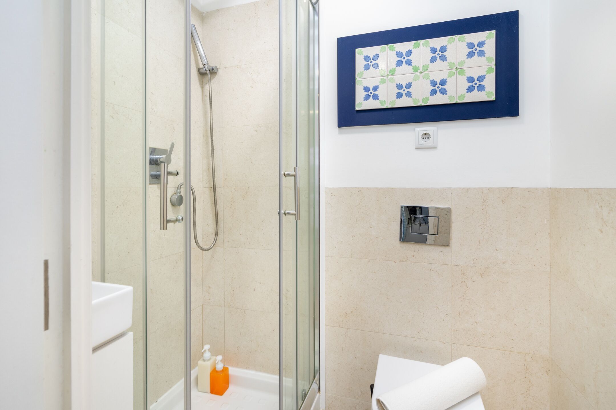 A glass-enclosed shower with a handheld showerhead, a white sink, and a towel rack.