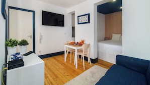 A compact living space with a dining area, a sofa, a TV mounted on the wall, and a bed.