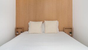 A bed with a wooden headboard, two bedside tables with small potted plants, and a white bedspread.