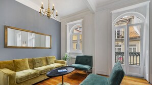 Ein Zimmer mit einem gelben Sofa, einem grünen Sessel, einem runden Tisch und einem großen Spiegel an der Wand.
