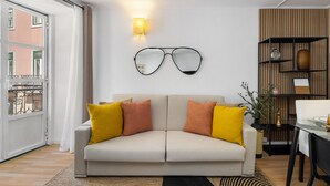 Ein modernes Wohnzimmer mit einem beigen Sofa, gelben und orangefarbenen Kissen, einer Wandlampe und einem Brillenschmuckstück.