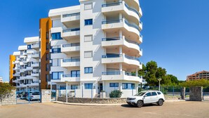 Un edificio residencial de varios pisos con balcones, entrada protegida por una reja y un coche estacionado.