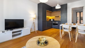 A modern living room with a flat-screen TV, a dining table with chairs, a kitchen area with a microwave, and a large mirror. - Urban Elegance: A Modern Haven In Lisbon'S Heart (Lisbon)