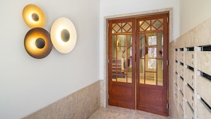 A hallway with a wooden door, a wall-mounted light fixture, and a marble floor. - Urban Elegance: A Modern Haven In Lisbon'S Heart (Lisbon)
