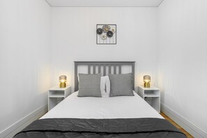 Un dormitorio moderno con una cama, dos mesitas de noche y una lámpara de pared.