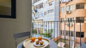 A balcony with a table set for breakfast, including pastries and orange juice, overlooking a residential area with multiple buildings. - Urban Elegance: A Modern Haven In Lisbon'S Heart (Lisbon)