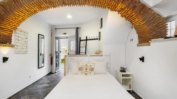 A bedroom with a white bed, a decorative ceiling, a white wall with a mirror, and a small white nightstand. - Cozy Alfama Haven: Perfect For Exploring Lisbon (Lisbon)