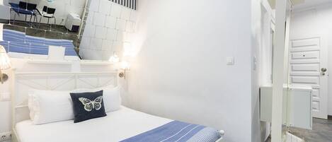 A hotel room with a bed, a desk with chairs, a bathroom with a shower, and a staircase.