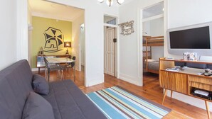 Un espace de vie compact comprenant un canapé, un coin repas, un téléviseur et un lit superposé.