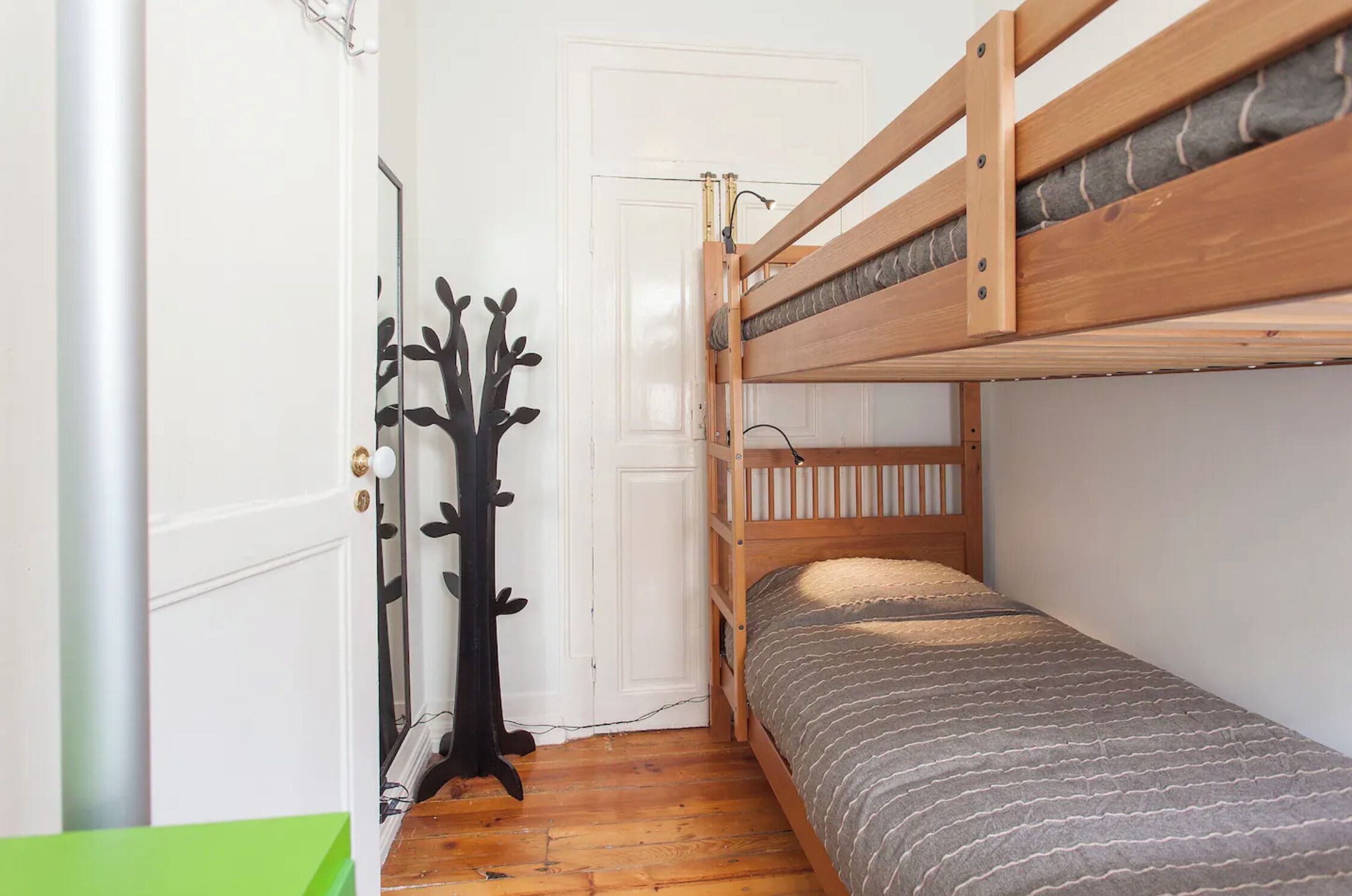 A bunk bed room with a wooden frame, a door with a black tree decoration, and a green wall.