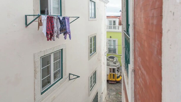 Une ruelle étroite entre deux immeubles, avec du linge suspendu à un fil, un tram jaune et une balustrade de balcon verte.