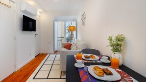 Ein modernes Hotelzimmer mit einem Flachbildfernseher, einem Esstisch mit Frühstück, einer Couch und einer Topfpflanze.