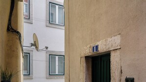 A narrow alleyway with a tiled floor leading to a building with a green door and a satellite dish. - Beco Patacas Perfect Location To Explore Lisbon (Lisbon)