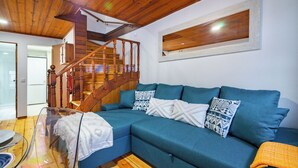 A modern living room with a wooden staircase, a blue sofa, and a glass coffee table. - Beco Patacas Perfect Location To Explore Lisbon (Lisbon)