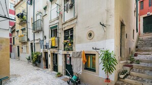 A narrow cobblestone street with buildings on either side, featuring balconies with laundry and potted plants. - Beco Patacas Perfect Location To Explore Lisbon (Lisbon)