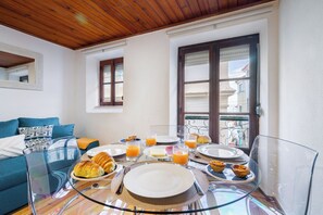 A breakfast setup with croissants, orange juice, and pastries on a glass table in a room with a wooden ceiling and a balcony view. - Beco Patacas Perfect Location To Explore Lisbon (Lisbon)