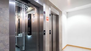 Un ascensore con un pannello di controllo digitale, un segnale di allarme antincendio e un pavimento piastrellato.