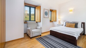 Una camera da letto con un letto, una sedia, una finestra e un comodino con una lampada.
